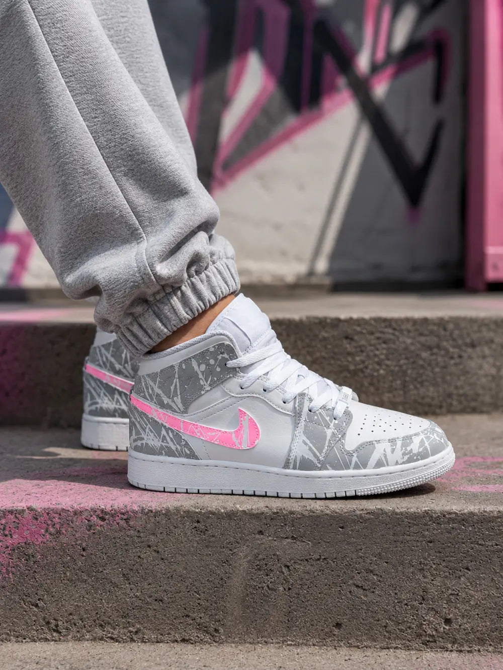 Air Jordan Low custom femme gris et rose fluo au style streetwear premium avec effet peinture abstraite et swoosh rose personnalisé.