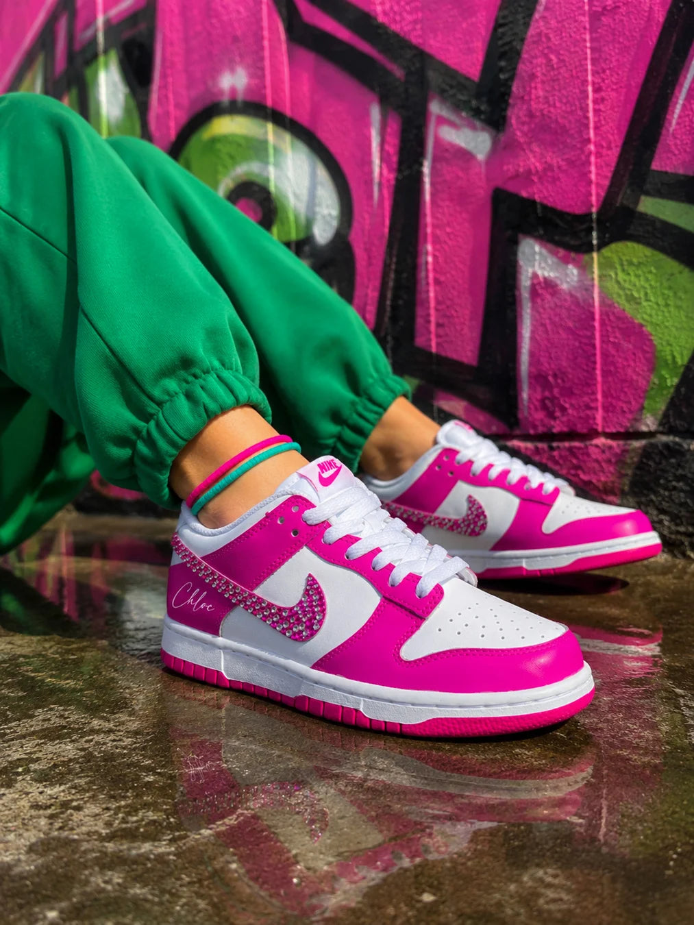 Nike Dunk Low personnalisée femme rose fuchsia avec swoosh en strass portée avec un jogging vert.