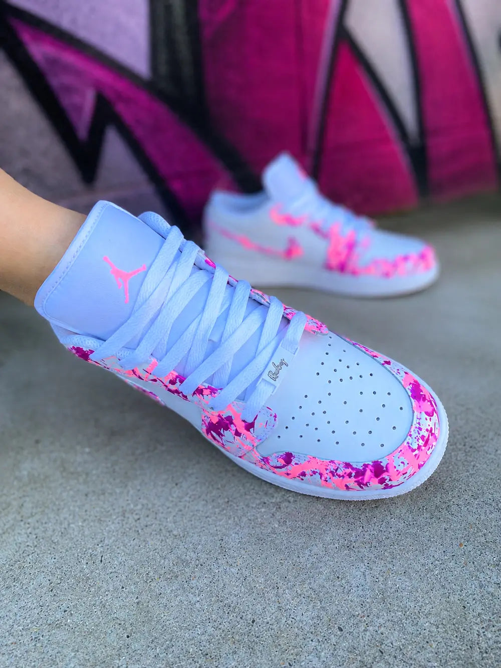 Zoom sur Air Jordan Low custom blanche avec éclaboussures rose néon et fuchsia, sneakers femme personnalisées style street art premium.
