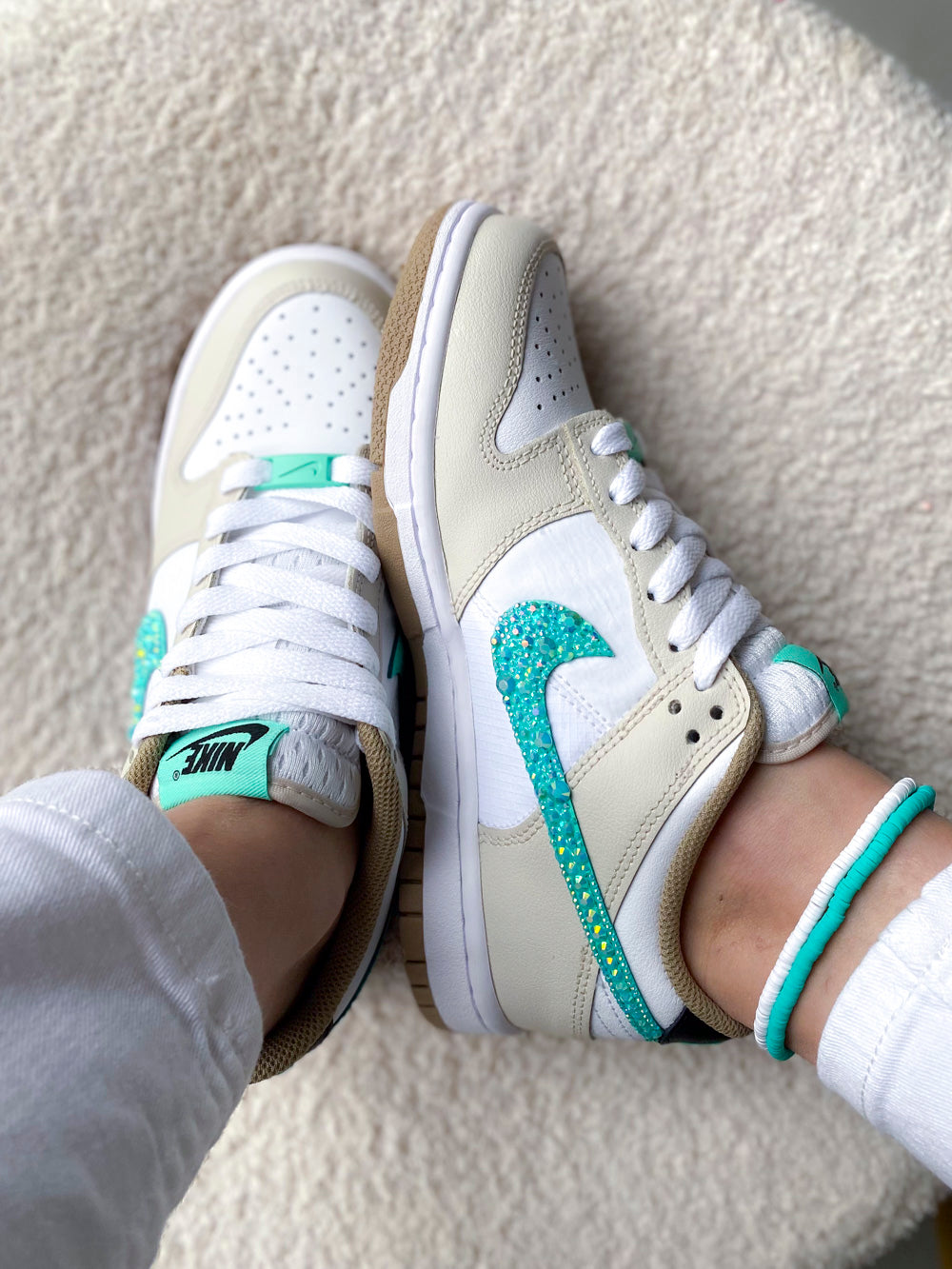 Cette image met en avant une paire de Nike Dunk Low femme beige et turquoise, agrémentée de strass pour un effet glamour