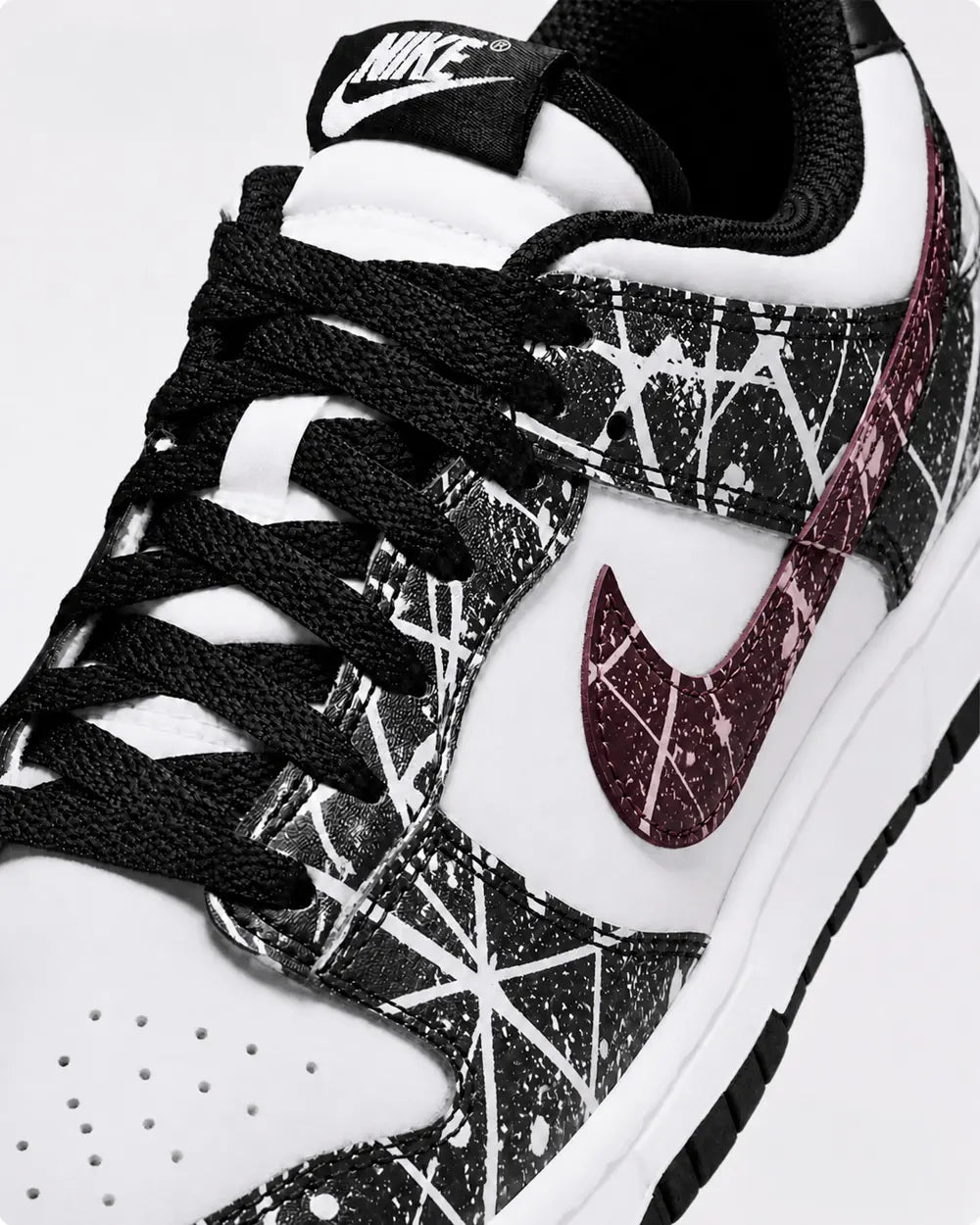 Zoom sur le swoosh bordeaux d’une Nike Dunk Low custom noire et blanche avec design paint splatter artistique fait main.