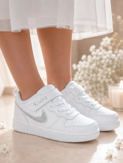 Baskets Nike blanches personnalisées pour enfant avec swoosh en strass argent, parfaites pour compléter une tenue de cérémonie.