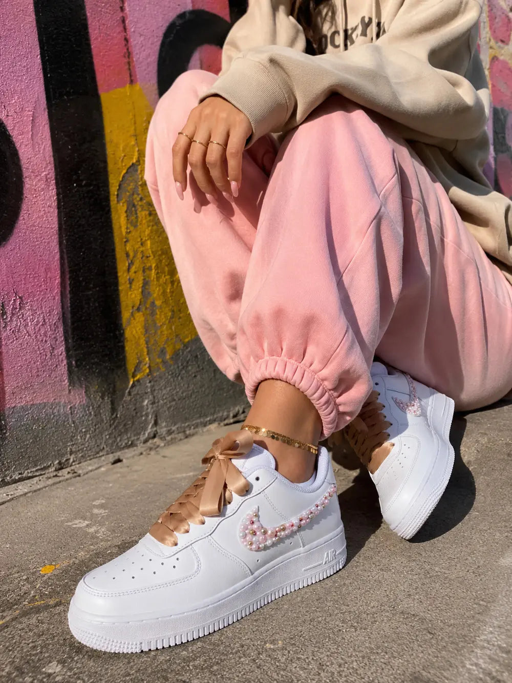 Basket custom femme Nike Air Force 1 avec lacets satin rose et swoosh perlé dans un décor graffiti streetwear tendance