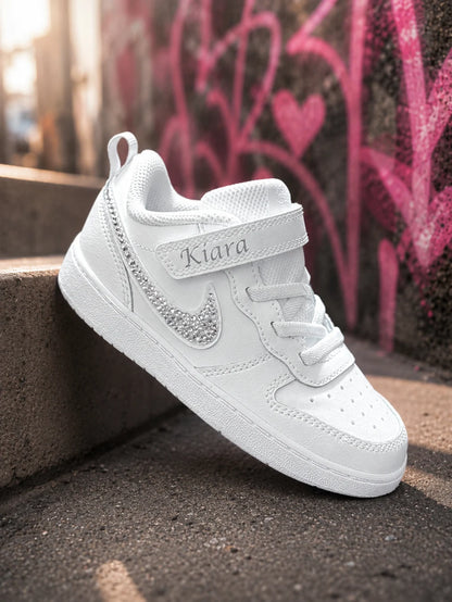 Basket Nike enfant personnalisée avec strass argent sur le swoosh, modèle blanc premium conçu pour une cérémonie, un baptême ou une tenue élégante.