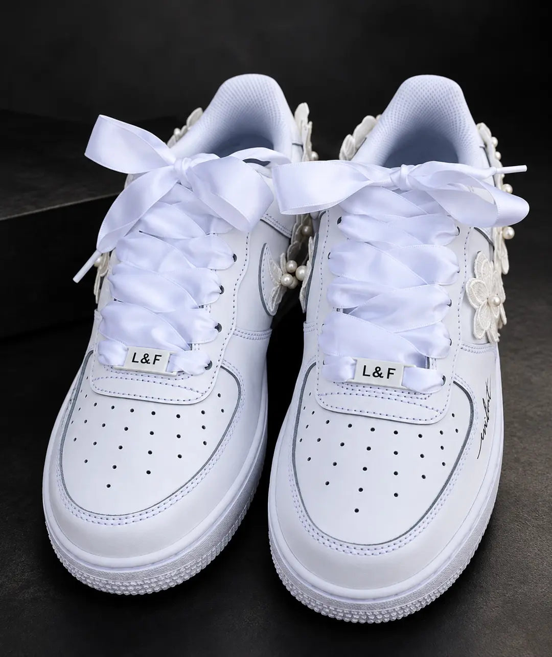 Baskets de mariée Nike Air Force 1 blanches avec lacets en satin noués, bijoux de chaussures personnalisés et fleurs brodées.