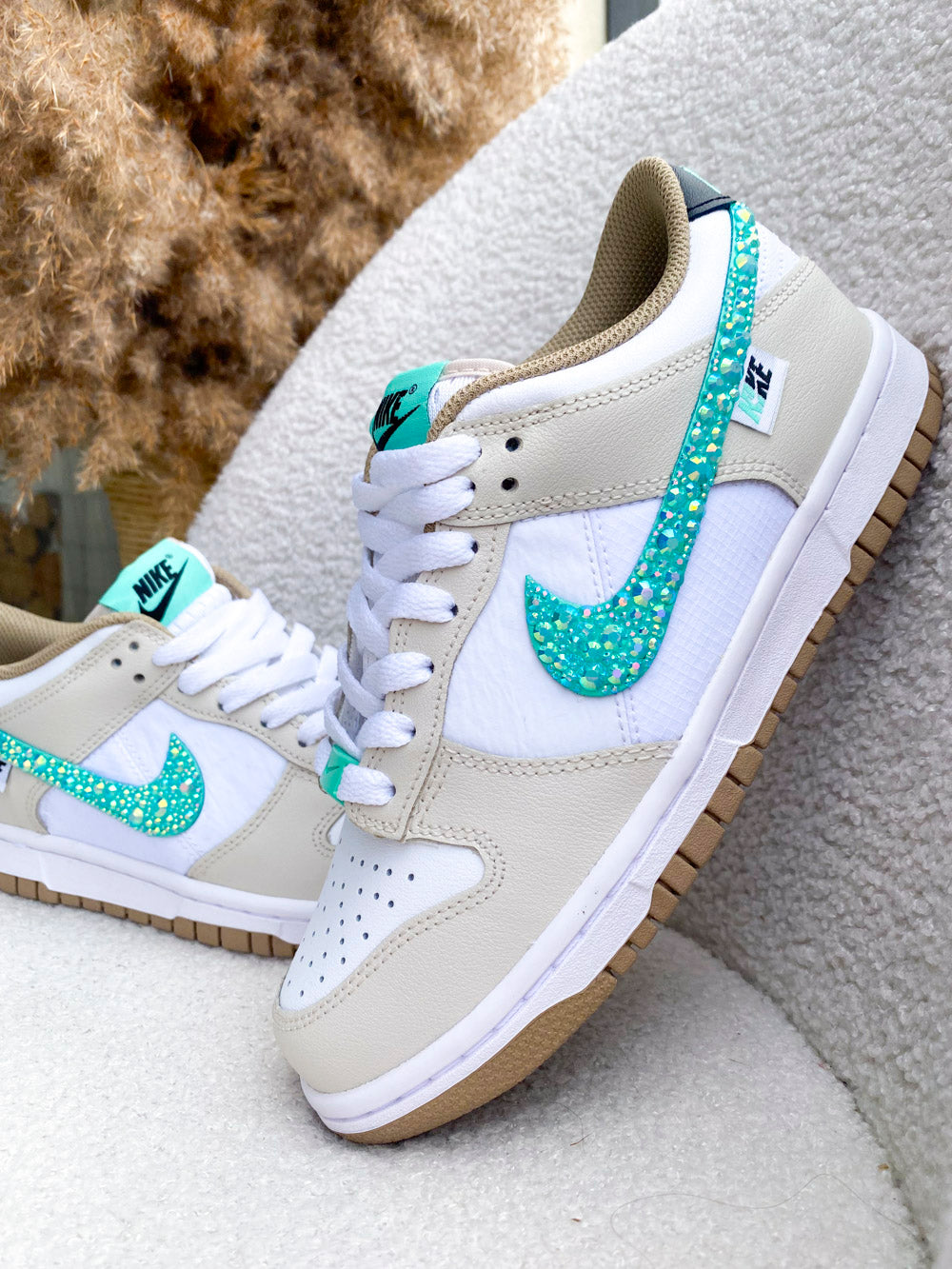 Sur la photo, une paire de Nike Dunk Low femme beige et turquoise, sublimée par des strass scintillants.