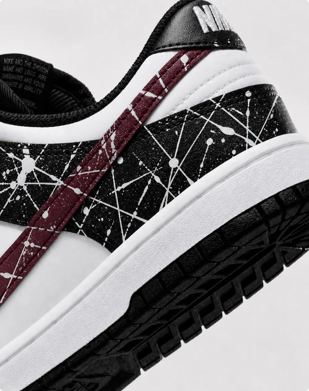 Détail arrière Nike Dunk Low custom noire et blanche avec swoosh bordeaux et effet éclaboussures peinture artisanales haut de gamme.