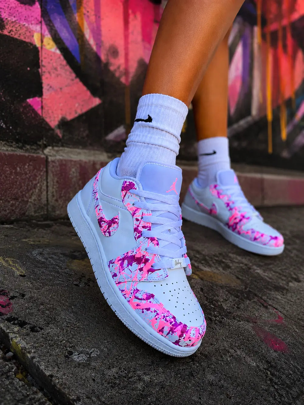 Air Jordan Low blanche custom rose fuchsia fluorescente portée en extérieur urbain, basket femme personnalisée style mode streetwear premium.