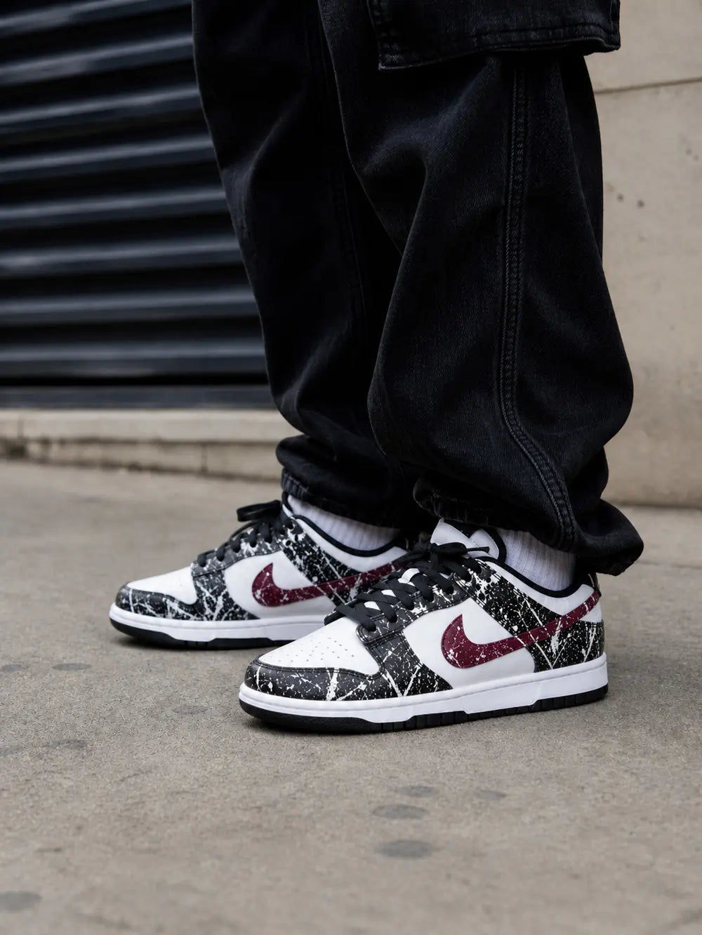 Nike Dunk Low personnalisée noir blanc et bordeaux avec effet paint splatter, basket custom premium streetwear mixte portée en milieu urbain.