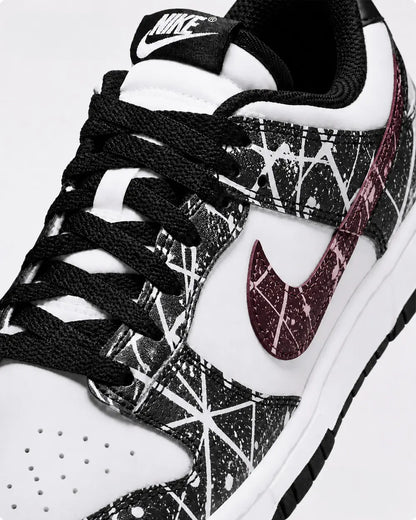 Zoom sur le swoosh bordeaux d’une Nike Dunk Low custom noire et blanche avec design paint splatter artistique fait main.